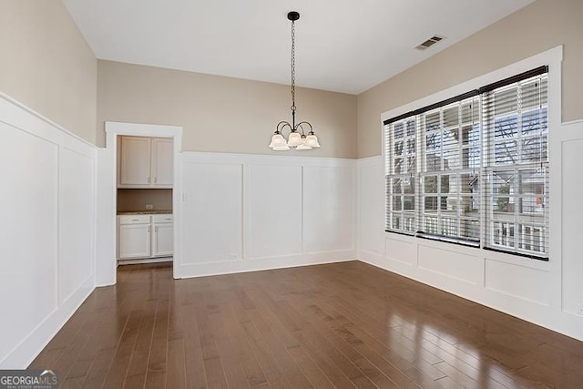 unfurnished dining area featuring a chandelier, a decorative wall, dark wood finished floors, and visible vents