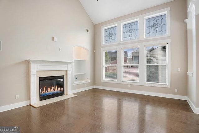 unfurnished living room with visible vents, high vaulted ceiling, a glass covered fireplace, baseboards, and dark wood-style flooring