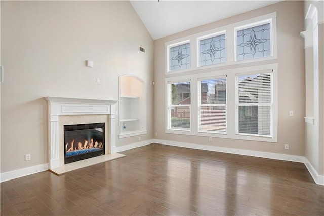 unfurnished living room with visible vents, dark wood-type flooring, a premium fireplace, baseboards, and high vaulted ceiling