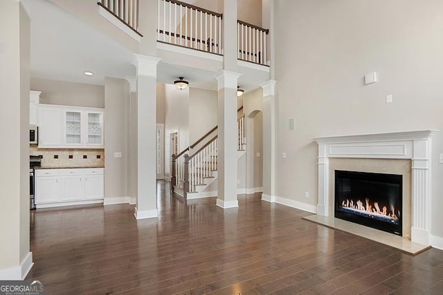 unfurnished living room featuring a glass covered fireplace, baseboards, dark wood-style flooring, and a towering ceiling