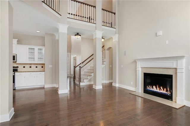 unfurnished living room featuring a high ceiling, dark wood-style flooring, and a glass covered fireplace