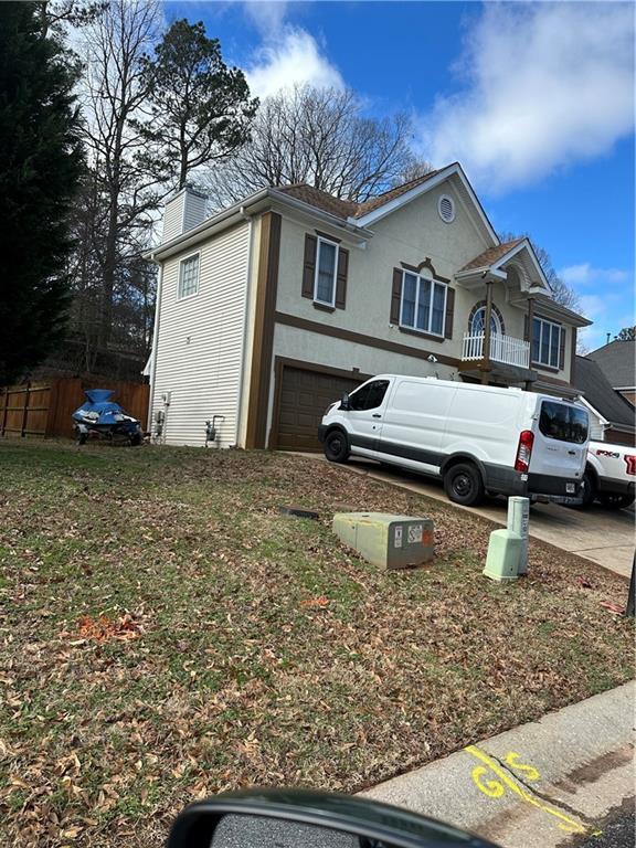 view of side of home featuring fence, stucco siding, a chimney, driveway, and an attached garage