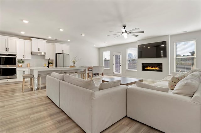 living room with a healthy amount of sunlight, light wood-style floors, recessed lighting, and a glass covered fireplace