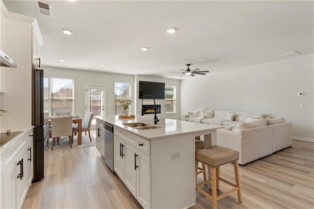 kitchen with visible vents, light wood-style floors, a kitchen breakfast bar, black appliances, and a sink