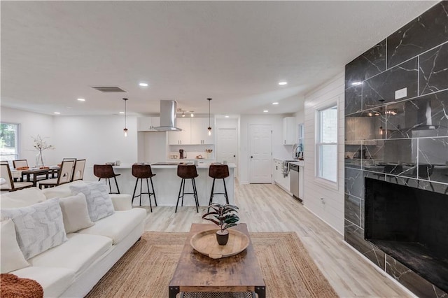 living room with light wood-type flooring, a high end fireplace, visible vents, and recessed lighting