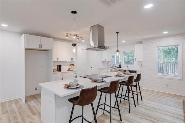 kitchen featuring light countertops, visible vents, white cabinets, island range hood, and black electric cooktop