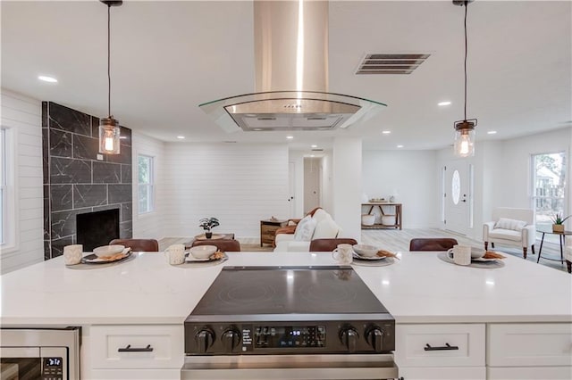 kitchen with wall chimney exhaust hood, visible vents, stainless steel appliances, and open floor plan