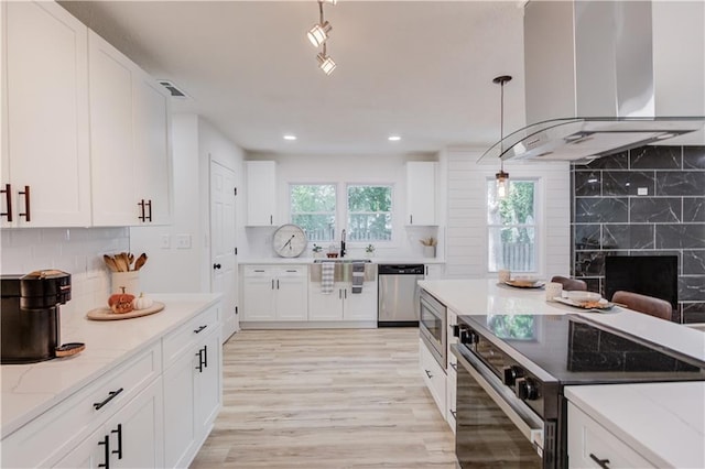 kitchen with white cabinets, light stone countertops, island range hood, and stainless steel appliances