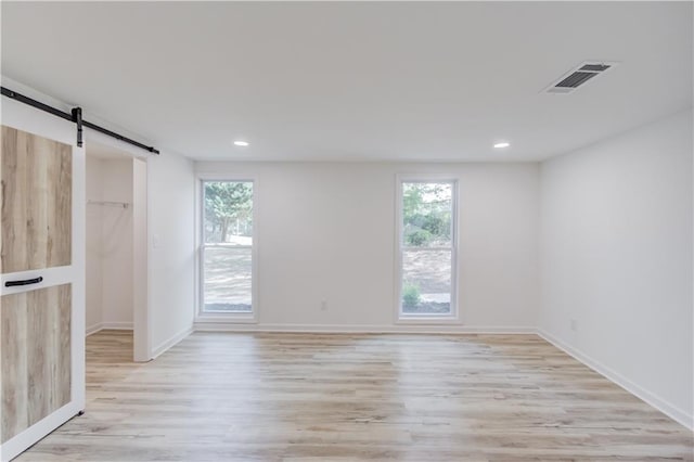 empty room with plenty of natural light, a barn door, visible vents, and wood finished floors