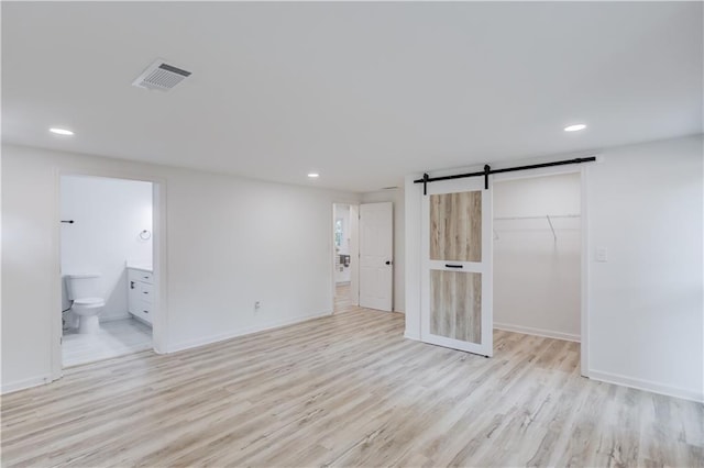 unfurnished bedroom featuring a walk in closet, visible vents, light wood-style flooring, and a barn door