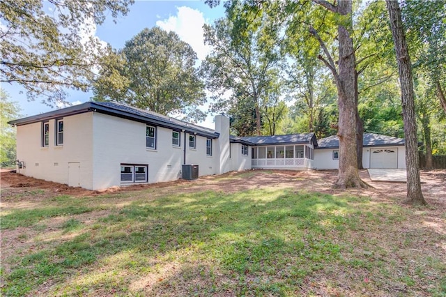 rear view of house featuring an attached garage, central air condition unit, a sunroom, a lawn, and a chimney