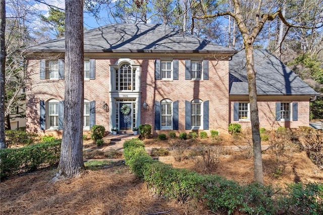 colonial inspired home featuring roof with shingles and brick siding