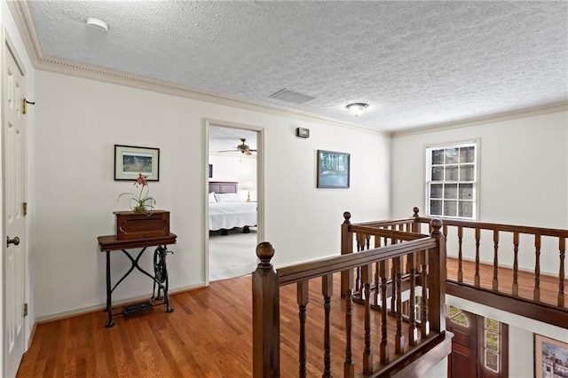 hall featuring a textured ceiling, wood-type flooring, and crown molding