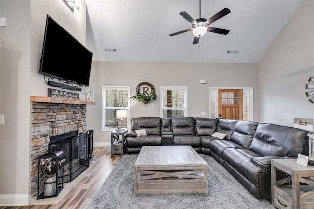 living room with visible vents, a ceiling fan, wood finished floors, a stone fireplace, and high vaulted ceiling