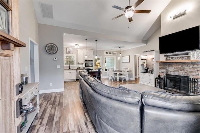 living room with a stone fireplace, visible vents, baseboards, a ceiling fan, and light wood finished floors