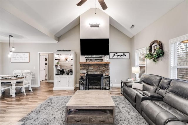 living area with visible vents, baseboards, light wood-type flooring, a fireplace, and high vaulted ceiling