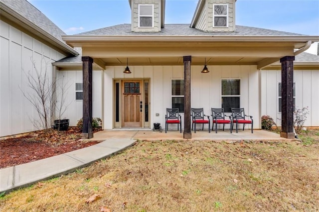 property entrance with board and batten siding, a lawn, a shingled roof, and a patio