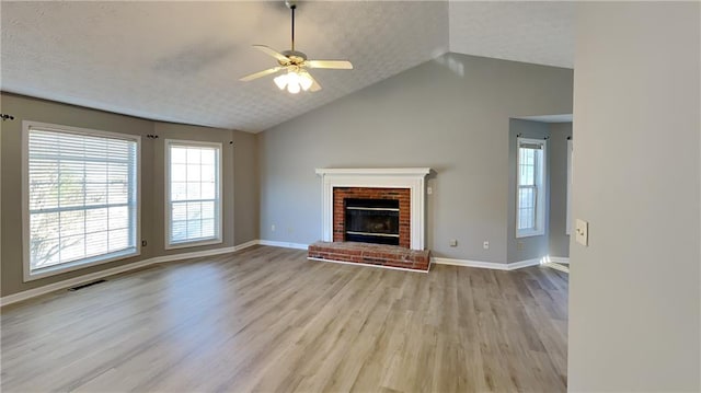 unfurnished living room featuring ceiling fan, lofted ceiling, light hardwood / wood-style floors, and a brick fireplace