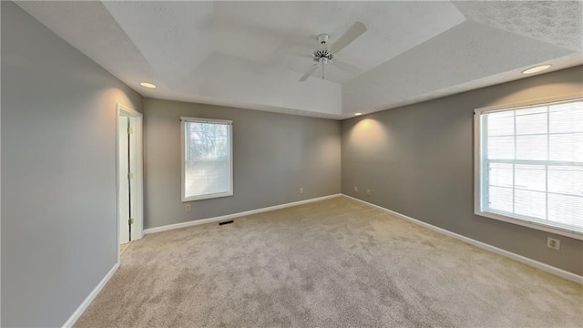 spare room featuring ceiling fan, light colored carpet, a tray ceiling, and a wealth of natural light