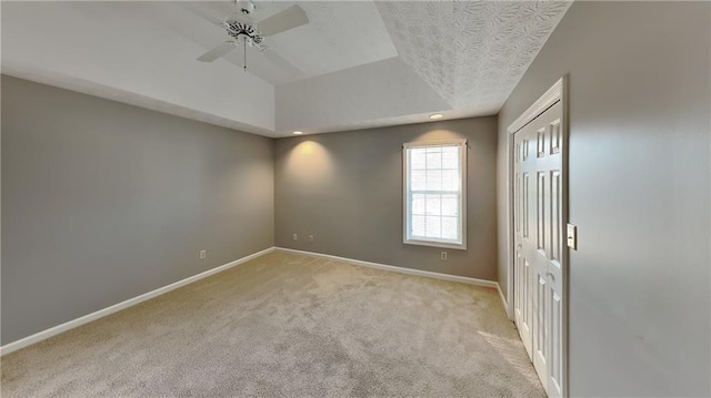 empty room featuring ceiling fan, light carpet, a textured ceiling, and a tray ceiling