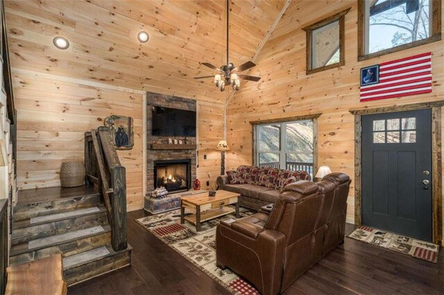 living room with high vaulted ceiling, wooden walls, a fireplace, ceiling fan, and dark wood-type flooring