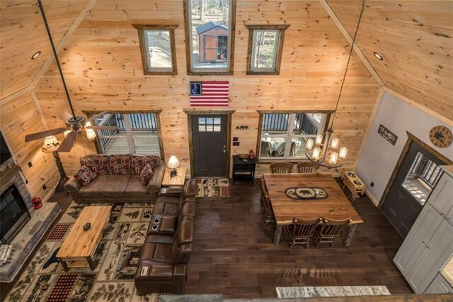 living room with ceiling fan, a towering ceiling, dark hardwood / wood-style flooring, and wood walls