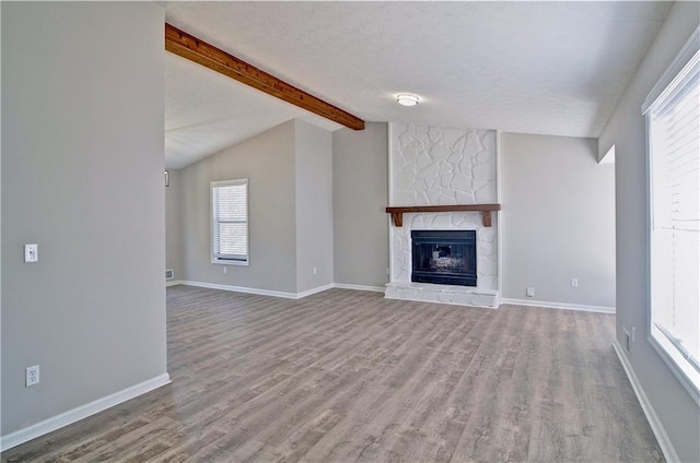 unfurnished living room featuring light wood-type flooring, vaulted ceiling with beams, a textured ceiling, and a stone fireplace