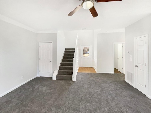 unfurnished living room featuring ceiling fan, crown molding, and dark colored carpet