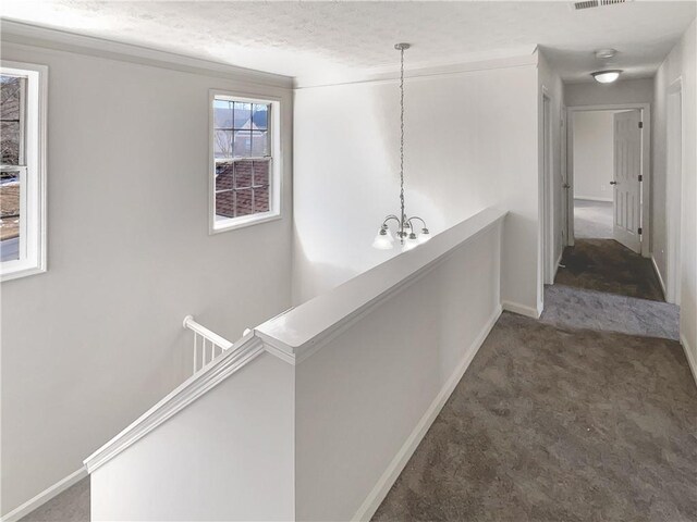 corridor featuring a textured ceiling, dark colored carpet, a healthy amount of sunlight, and an inviting chandelier