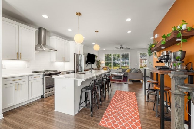 kitchen with white cabinets, stainless steel appliances, a kitchen island with sink, and wall chimney range hood