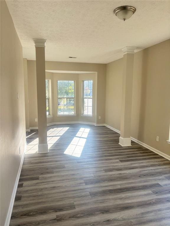 empty room featuring ornate columns, dark hardwood / wood-style floors, and a textured ceiling