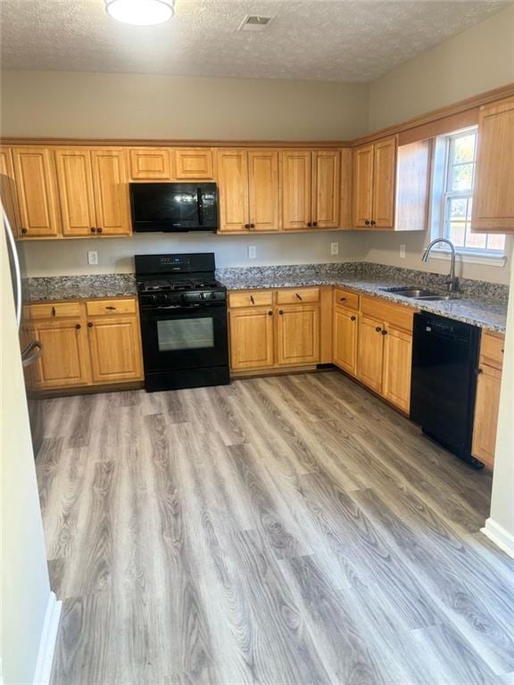 kitchen featuring light wood-type flooring, sink, a textured ceiling, and black appliances