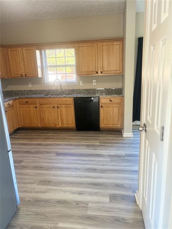 kitchen featuring black dishwasher, sink, light hardwood / wood-style flooring, and stone counters