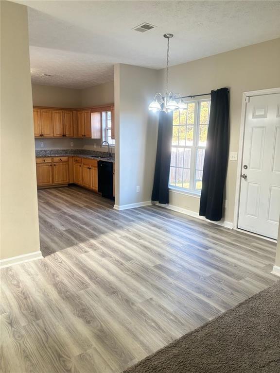 kitchen featuring pendant lighting, sink, black dishwasher, a notable chandelier, and light hardwood / wood-style flooring