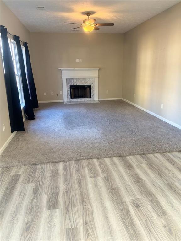 unfurnished living room with ceiling fan, light wood-type flooring, and a high end fireplace