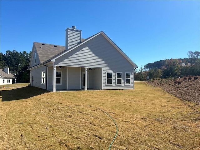 rear view of house featuring a yard, a chimney, and ceiling fan