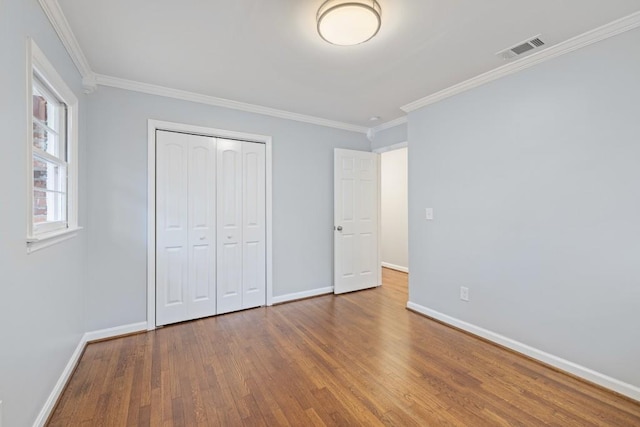 unfurnished bedroom with hardwood / wood-style flooring, ornamental molding, and a closet