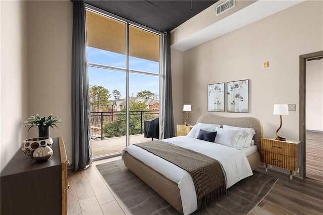 bedroom with access to exterior, wood-type flooring, and a wall of windows