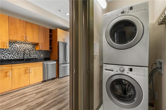 laundry area featuring stacked washer / drying machine, light hardwood / wood-style flooring, and sink