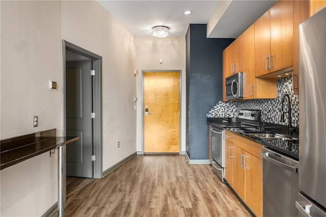 kitchen featuring appliances with stainless steel finishes, sink, dark stone counters, decorative backsplash, and light hardwood / wood-style flooring