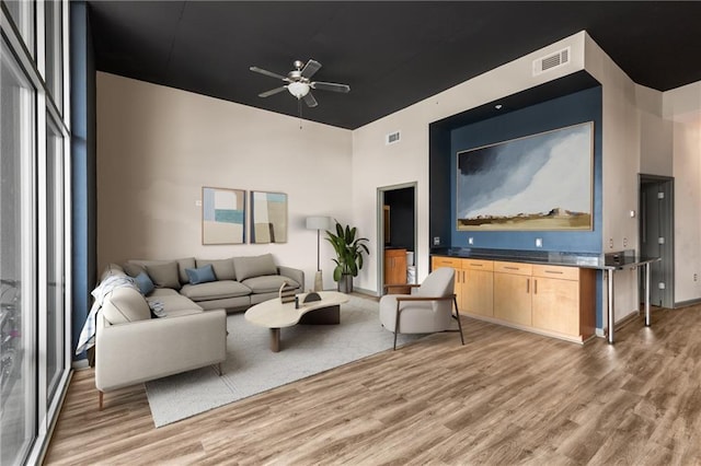 living room with a high ceiling, ceiling fan, and light hardwood / wood-style flooring