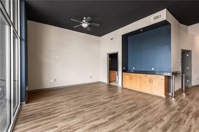 unfurnished living room featuring a high ceiling, ceiling fan, and light wood-type flooring