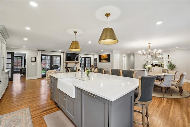 kitchen with a center island with sink, a sink, ornamental molding, gray cabinetry, and french doors