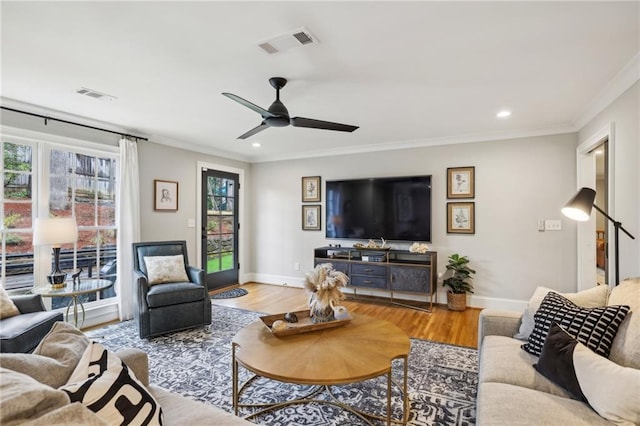 living area with crown molding, wood finished floors, visible vents, and baseboards