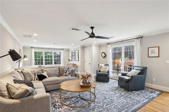 living area with visible vents, baseboards, wood finished floors, and crown molding