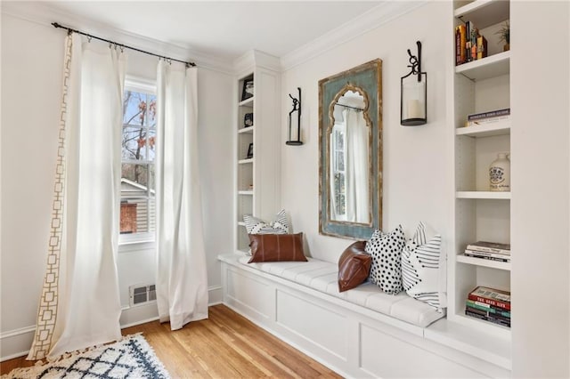 sitting room with visible vents, built in shelves, light wood-type flooring, and crown molding