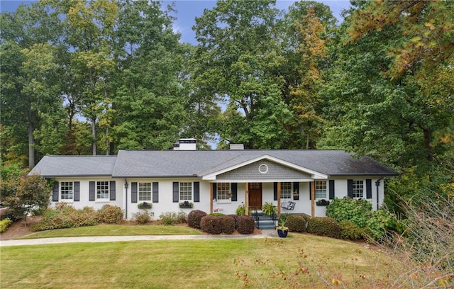 ranch-style house featuring covered porch, a chimney, and a front lawn