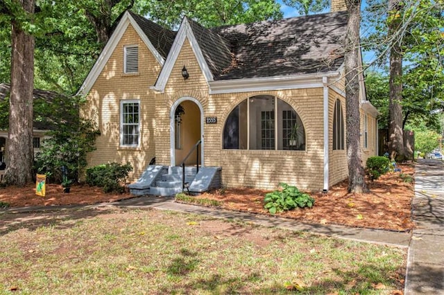 tudor-style house featuring a chimney and brick siding