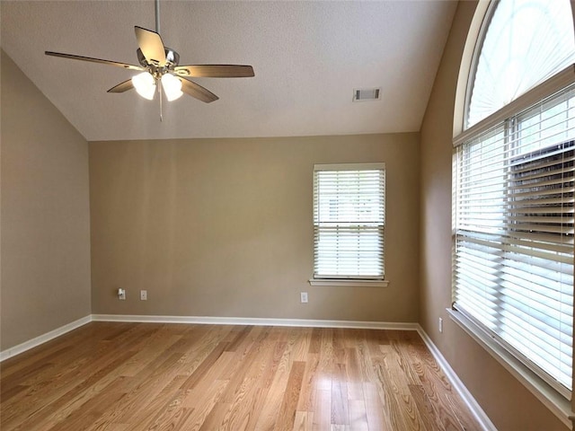spare room featuring lofted ceiling, visible vents, light wood finished floors, and a healthy amount of sunlight