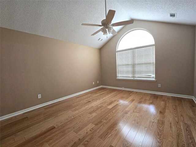 unfurnished room with a ceiling fan, wood finished floors, a textured ceiling, lofted ceiling, and visible vents
